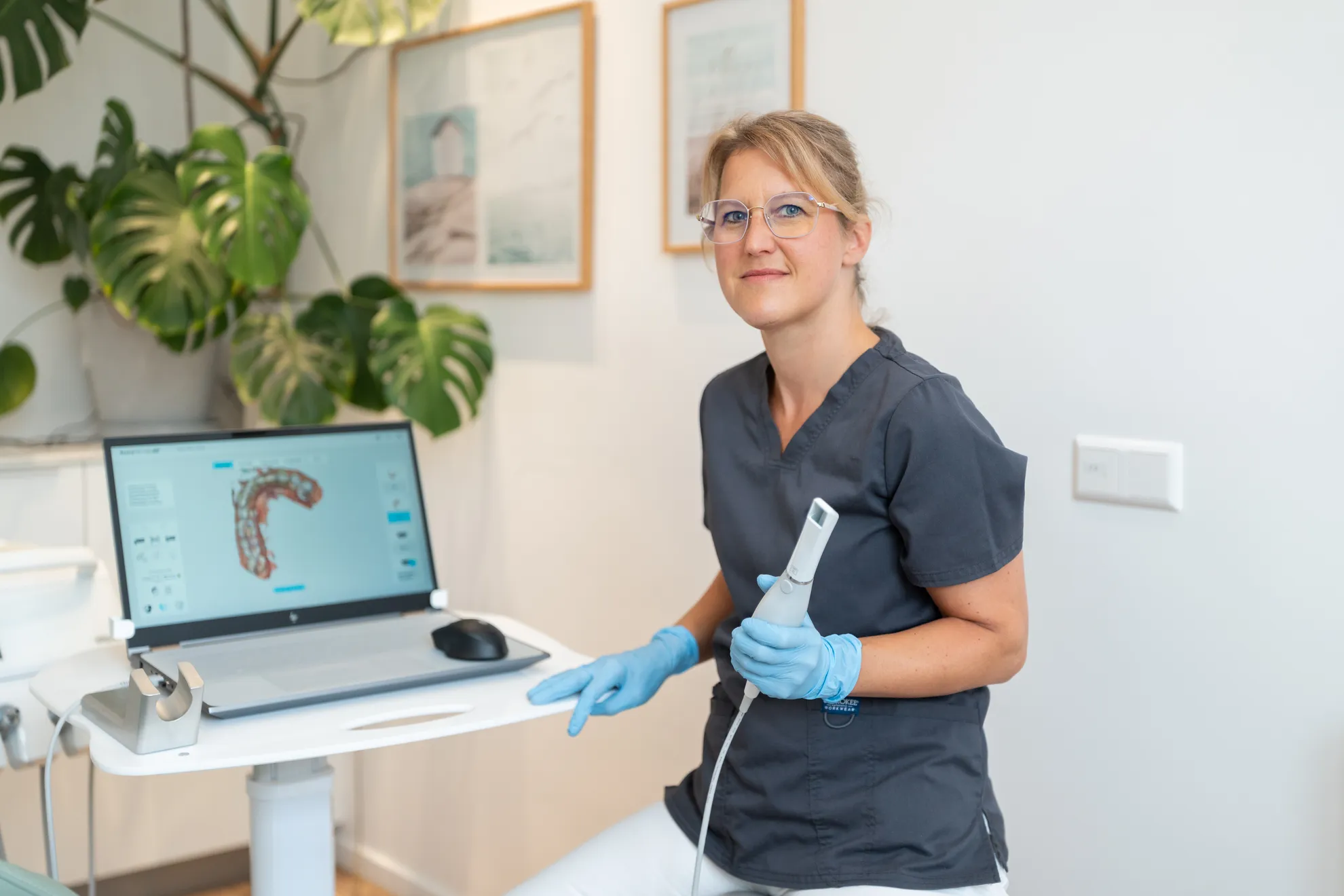 Kollegin im Behandlungsraum mit Werkzeug in der Hand und einem 3D-Bild vom Gebiss auf dem Bildschirm