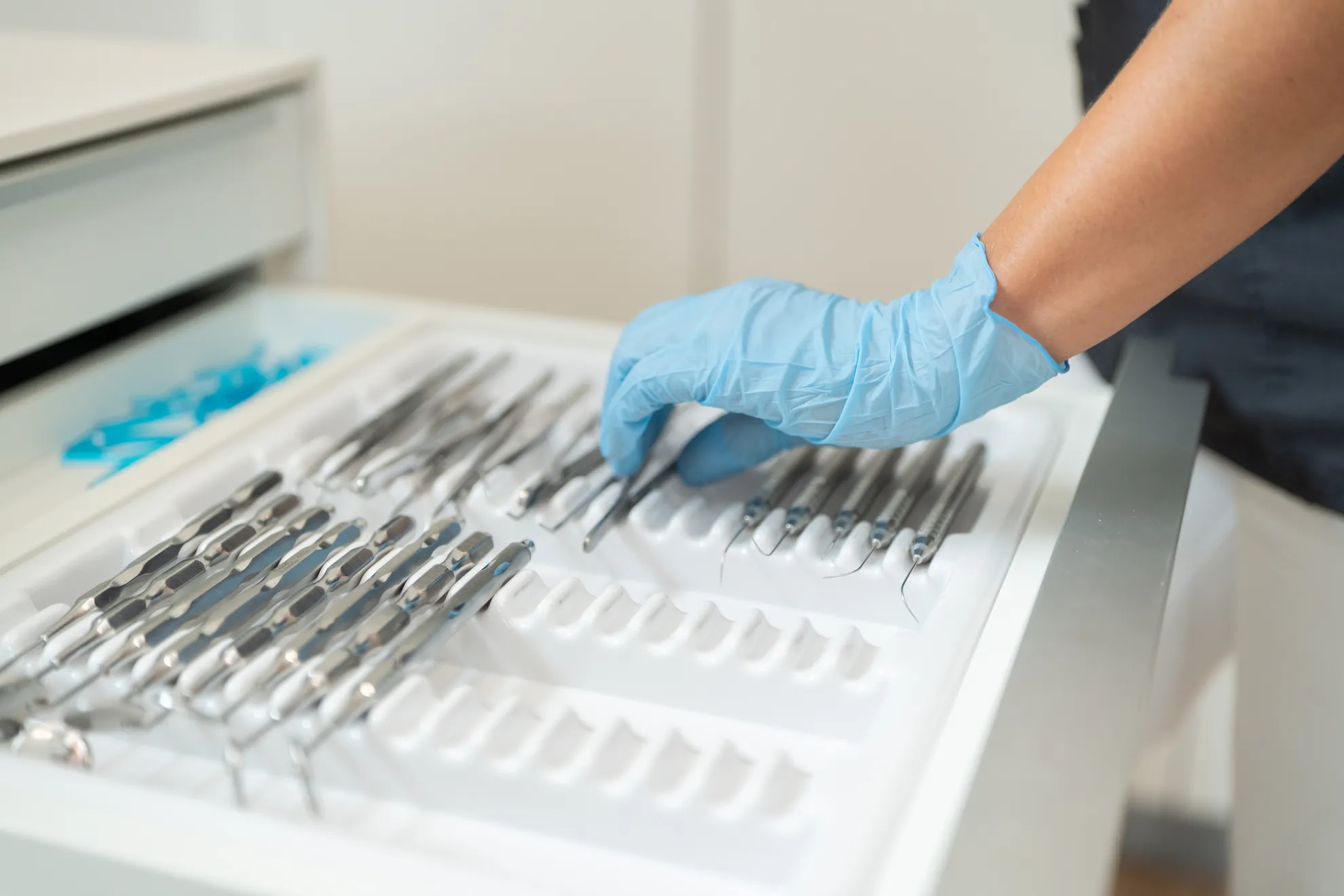 Blaue behandschuhte Hand legt Dentalinstrumente in Schublade
