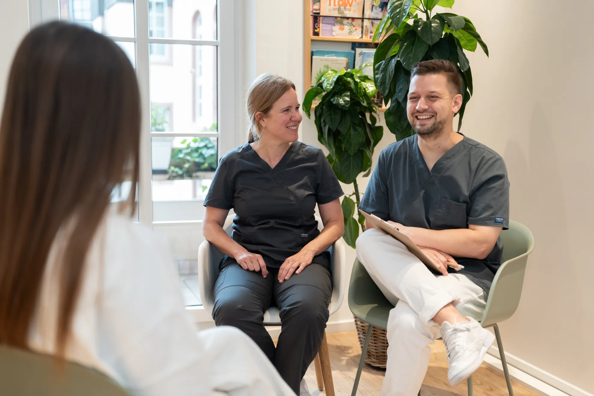 Zwei Zahnärzte posieren lächelnd in der Praxis mit einem Patienten