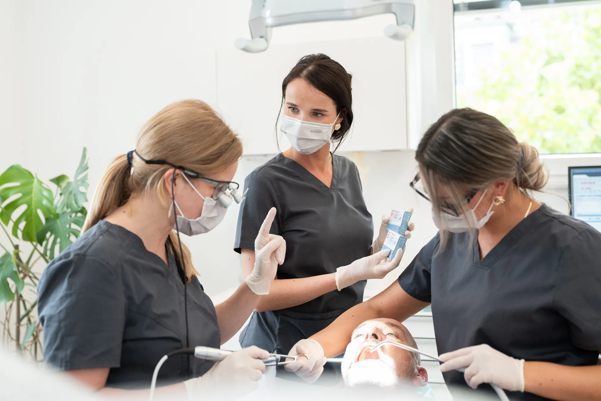 Zahnärztin und 2 ZFAs während einer zahnärztlichen Behandlung an einem Patienten